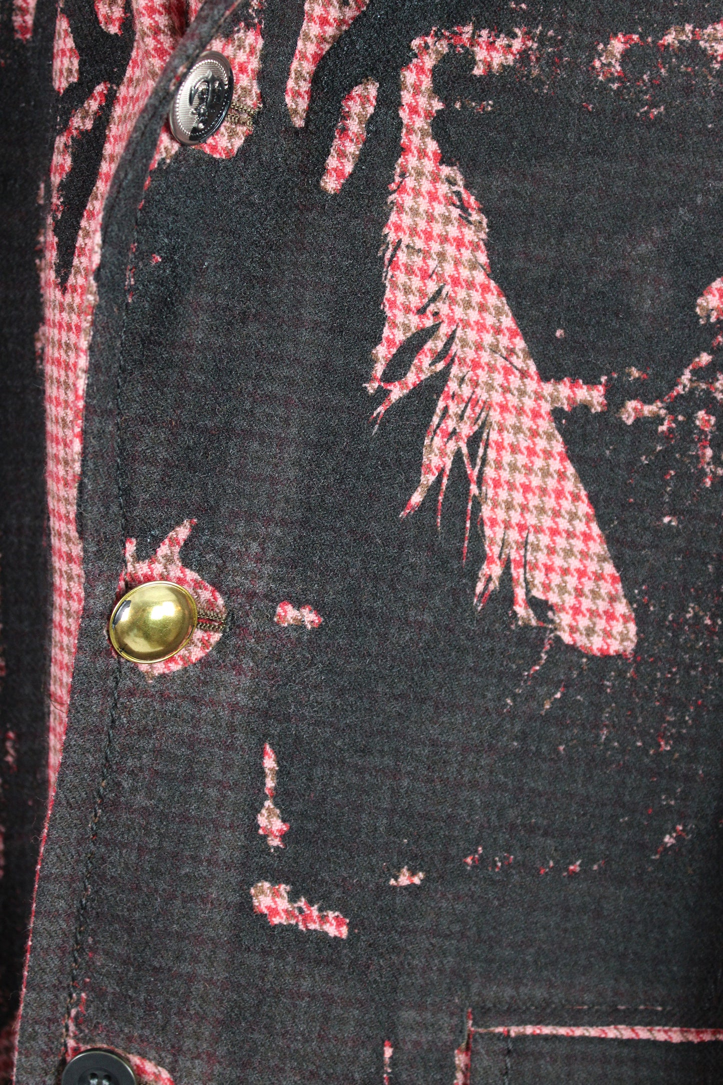 Close-up of a textured fabric with red checkered pattern and gold button on black background